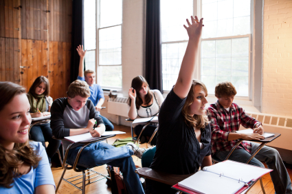 High School students in a classroom raising their hands.