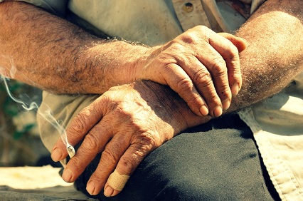 Image shows the hands of a hard working man as he enjoys his cigarette