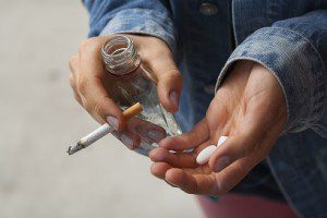 Young woman smoking cigarettes, drinking vodka and taking pills